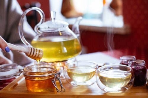 A glass teapot and cups of tea served with honey