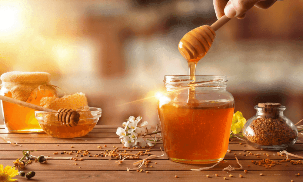 A honey dipper lifted over a jar, with honeycomb alongside