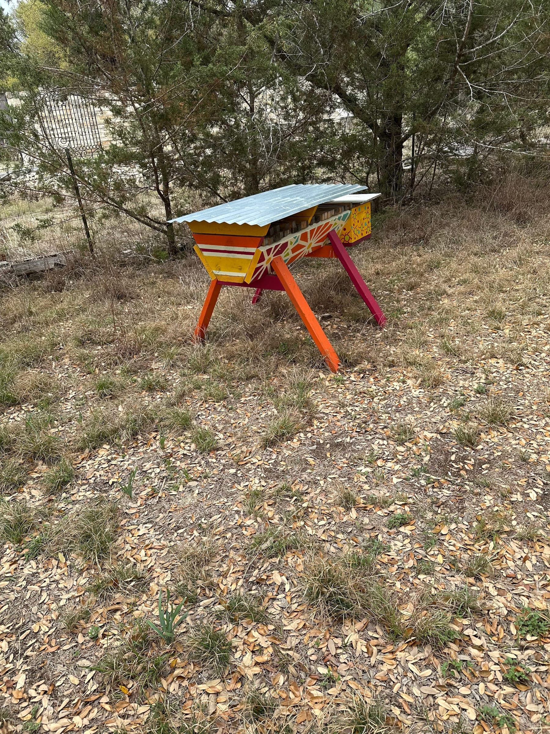 A painted top-bar hive on a stand outdoors