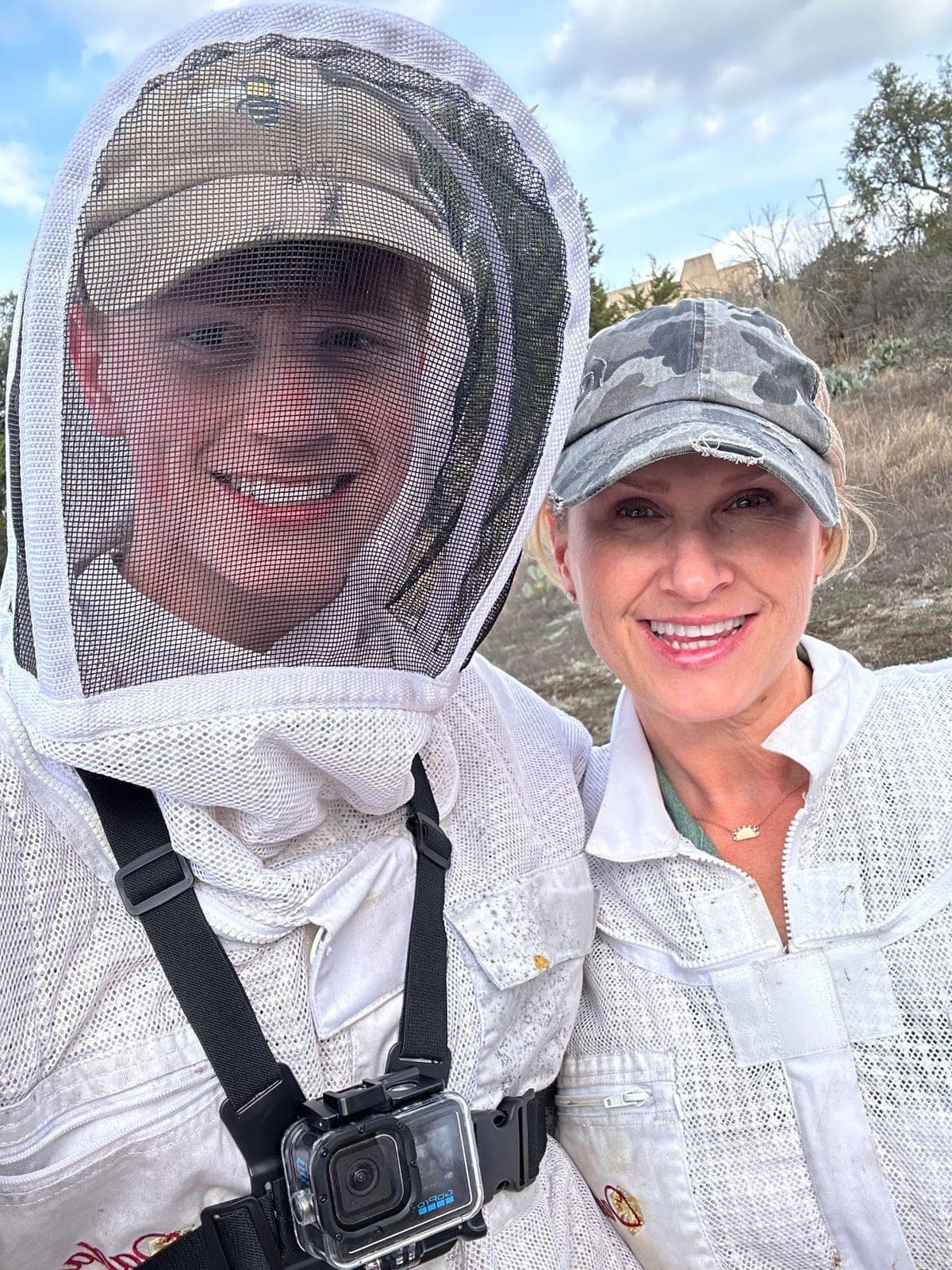 Joshua and Esther Davis in bee suits out on a job, Joshua in a mesh veil with a camera strapped to his chest