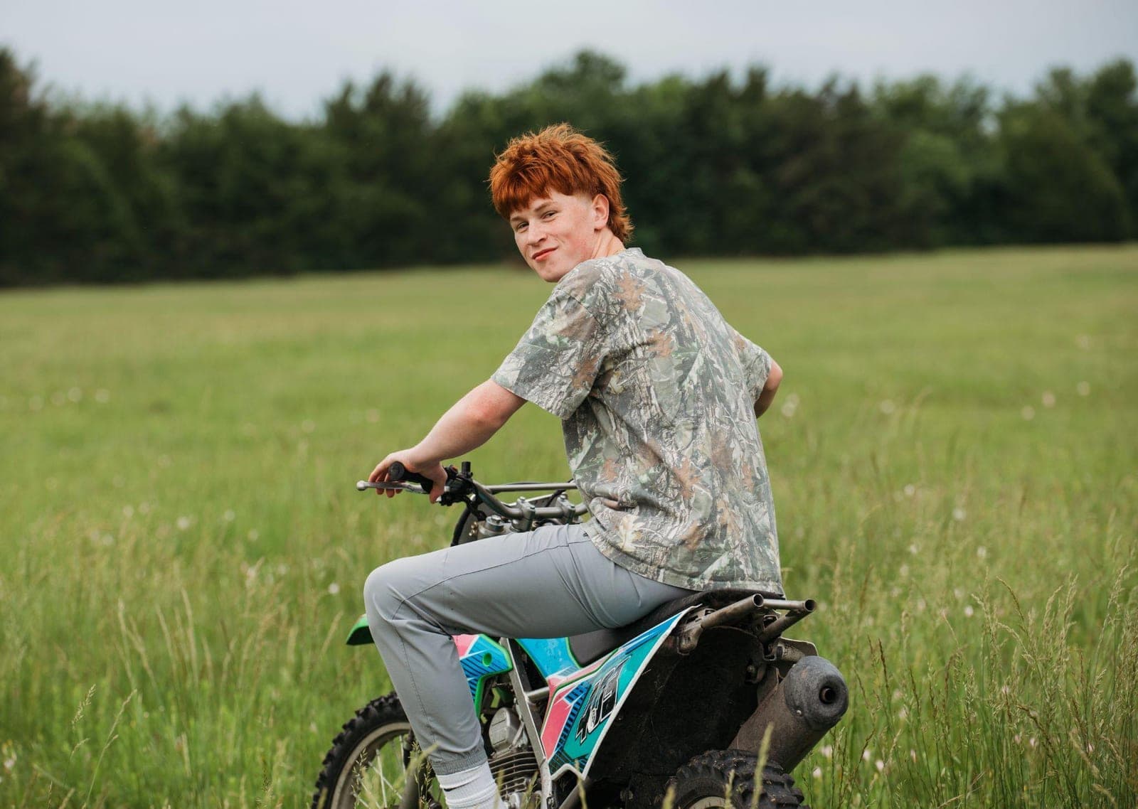 Joshua Davis sitting on his dirt bike in a grass field, looking back over his shoulder